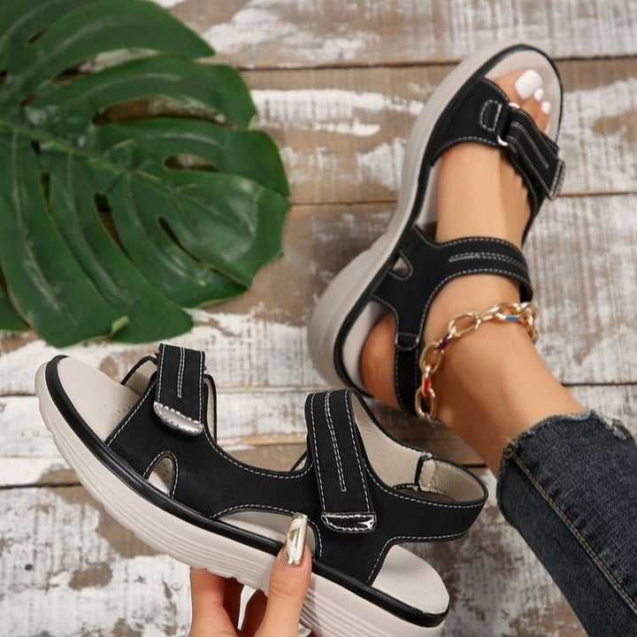 Black Xaviera adjustable platform sandals with contrast stitching, shown on a foot with an ankle bracelet.
