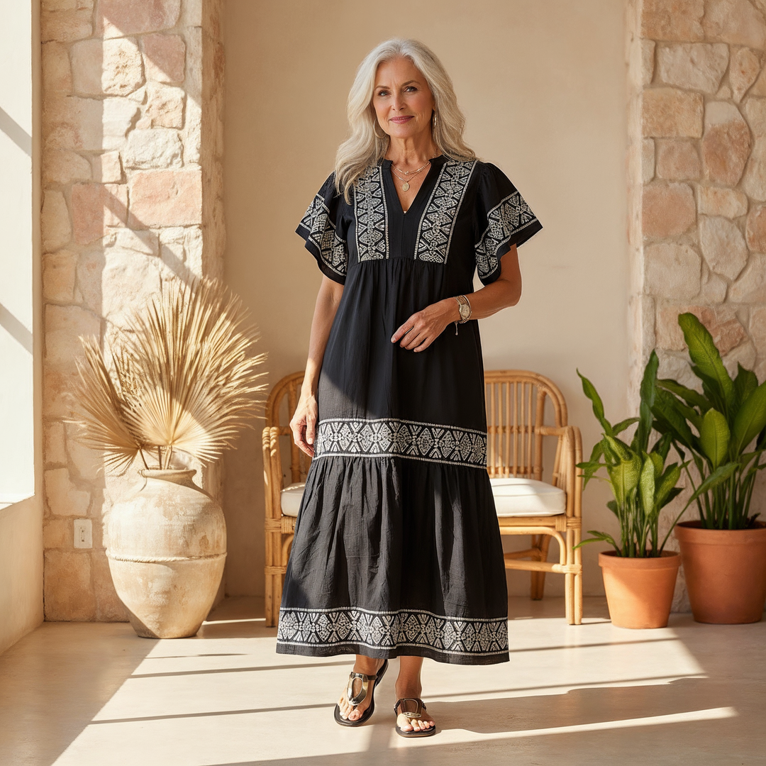 Woman in black Abigail boho V-neck midi dress with white embroidery, styled with sandals.