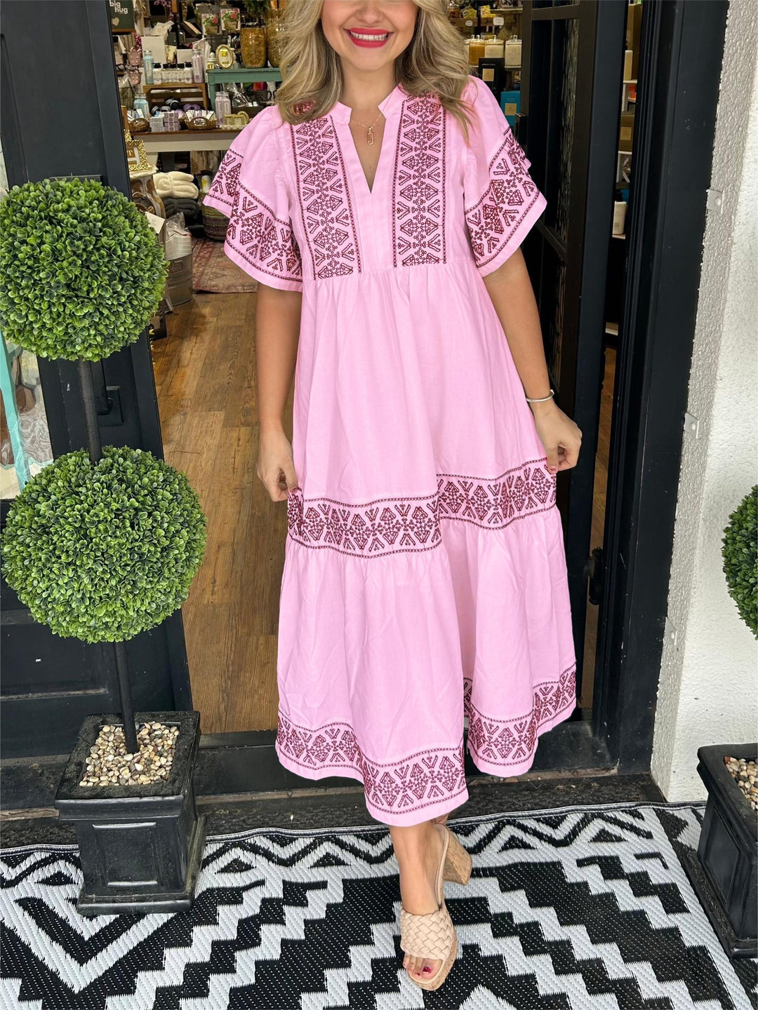 Woman in a pink Abigail boho V-neck midi dress with intricate brown embroidery, styled with nude sandals.