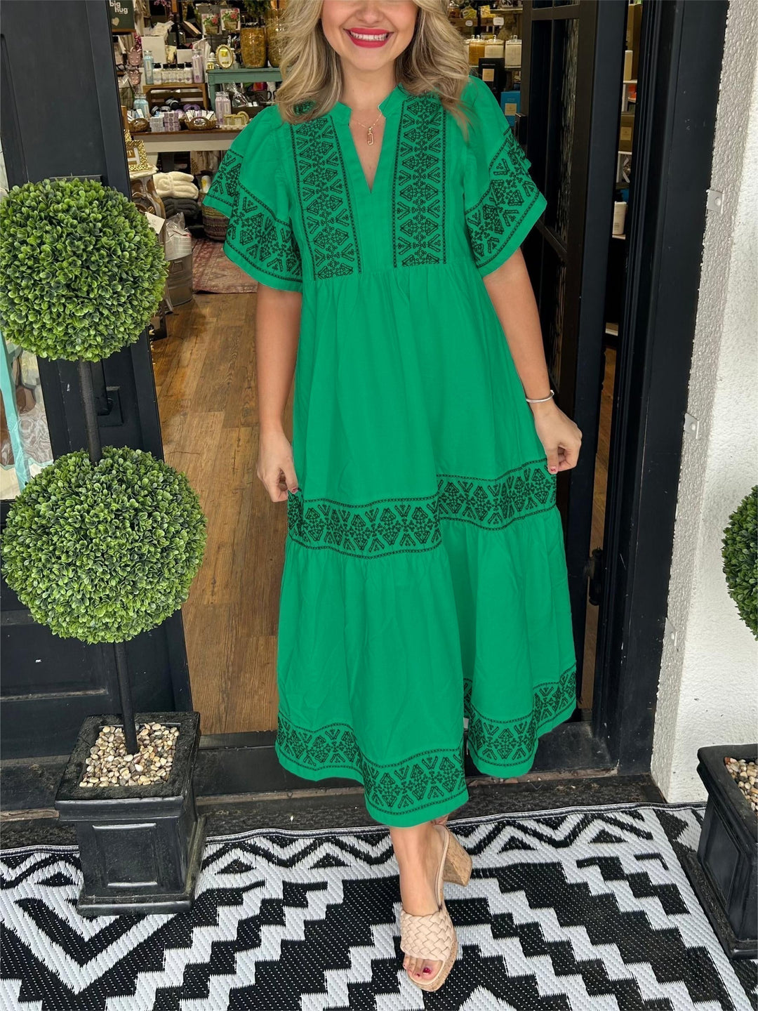 Woman in a vibrant green Abigail boho V-neck midi dress with black embroidered details, tiered skirt, and short sleeves.