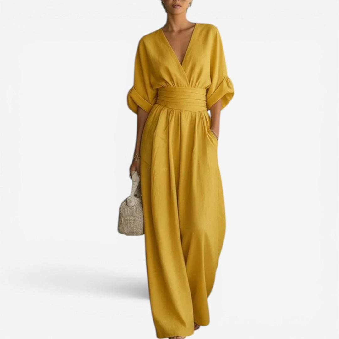 Mustard yellow V-neck jumpsuit with wide sleeves, a cinched waist, and flowing wide-leg trousers.