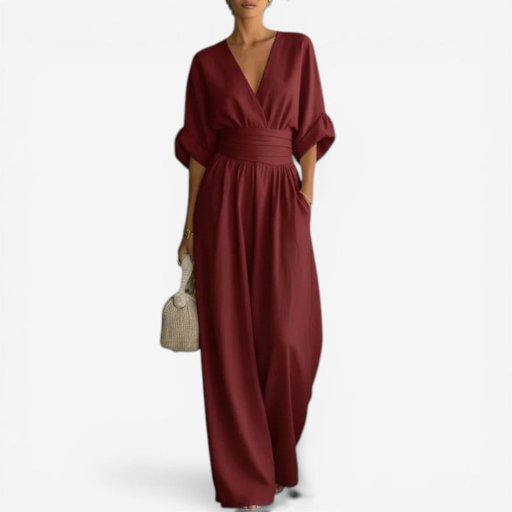Burgundy V-neck jumpsuit with wide sleeves, a cinched waist, and flowing wide-leg trousers.