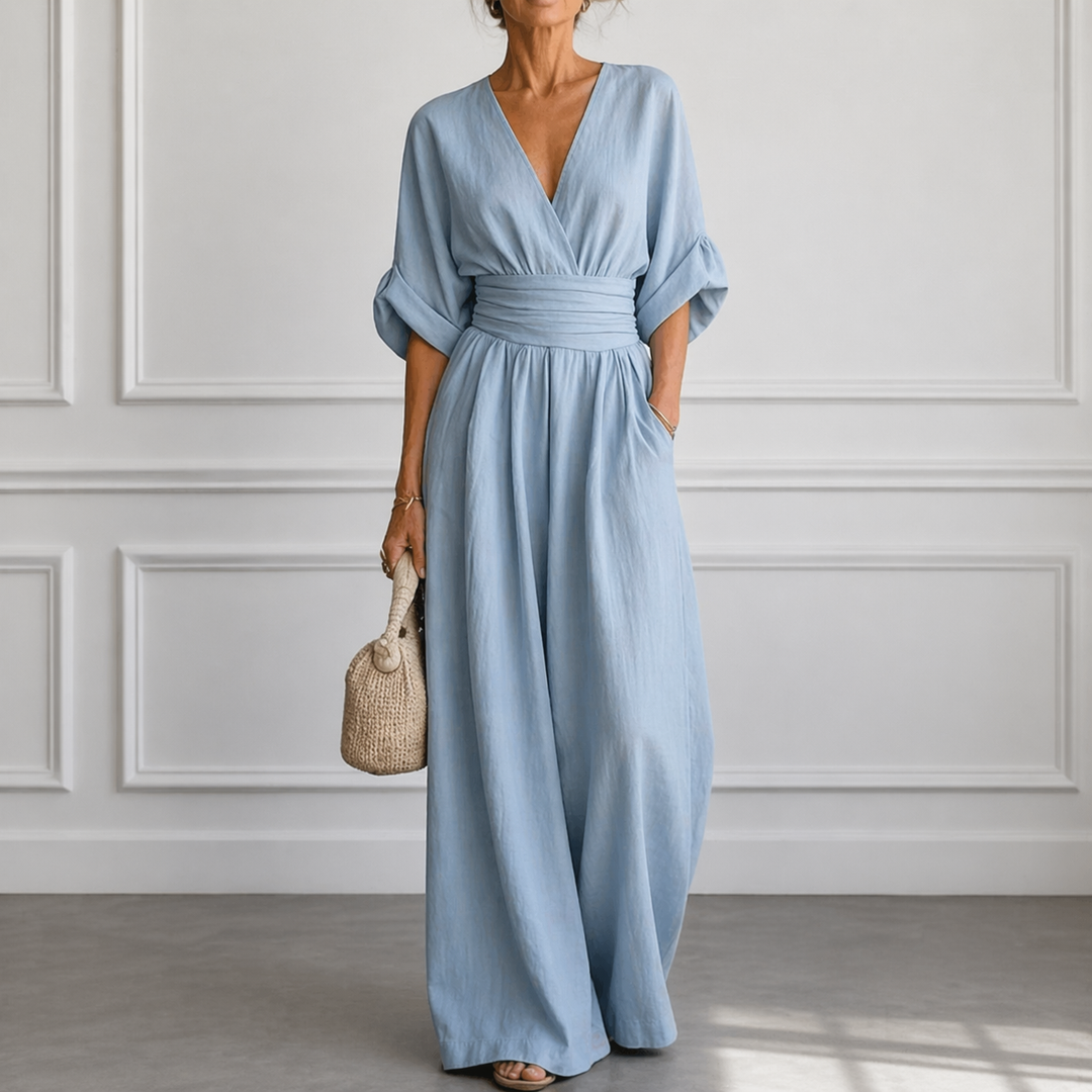 Light blue wide-leg V-neck jumpsuit with cinched waist and airy sleeves, styled with a woven handbag.