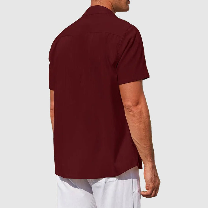 Men's Asher short sleeve linen button-up shirt in deep burgundy with subtle textured stripes, worn with white shorts.