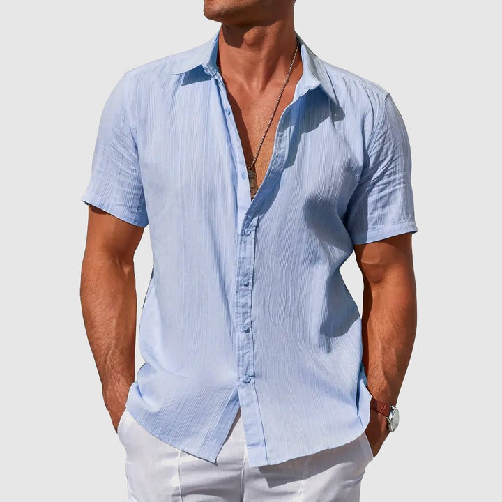 Men's Asher light blue short sleeve linen button-up shirt with subtle textured stripes, worn open over white pants.