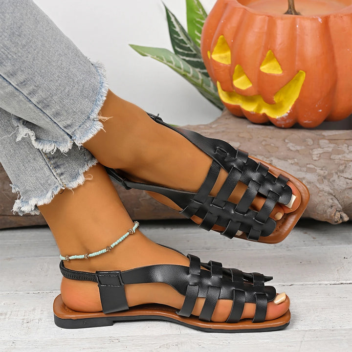 Black woven fisherman flat sandals with a slingback strap on feet, paired with frayed denim.