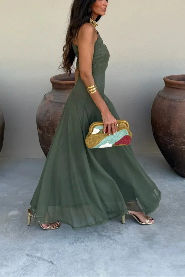 Woman in an olive green Aviana one-shoulder maxi dress, gold heels, and a colorful clutch.