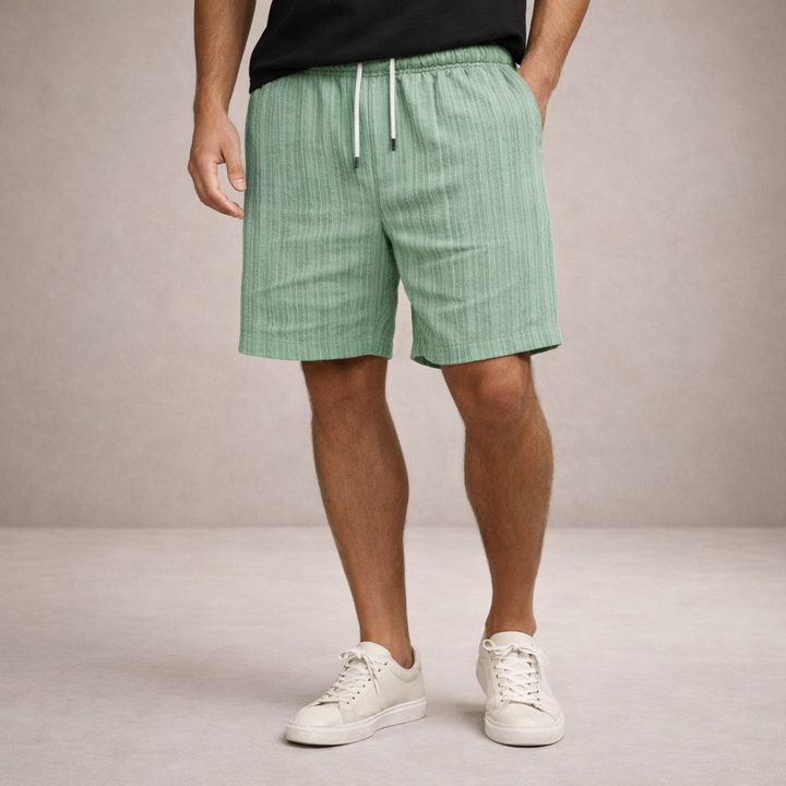Men's light green textured linen drawstring summer shorts with side pockets, styled with a black tee and white sneakers.