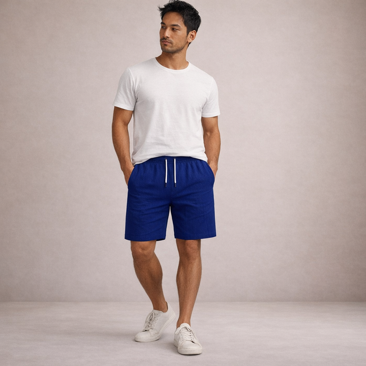 Man wearing royal blue linen drawstring shorts with a white tee and sneakers.