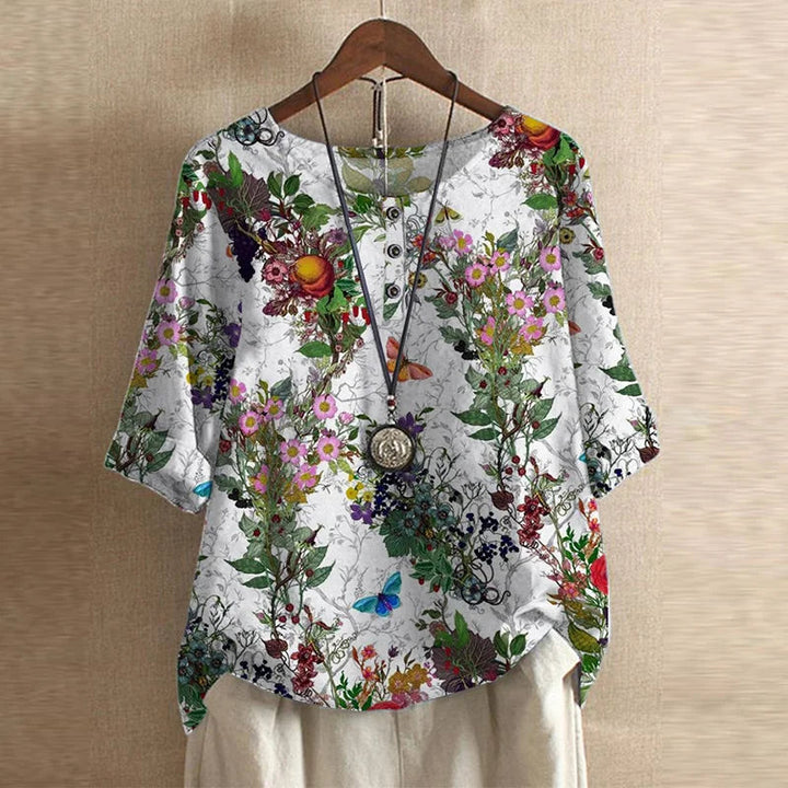 Women's white blouse featuring a vibrant floral print, three-quarter sleeves, and a button-front neckline.