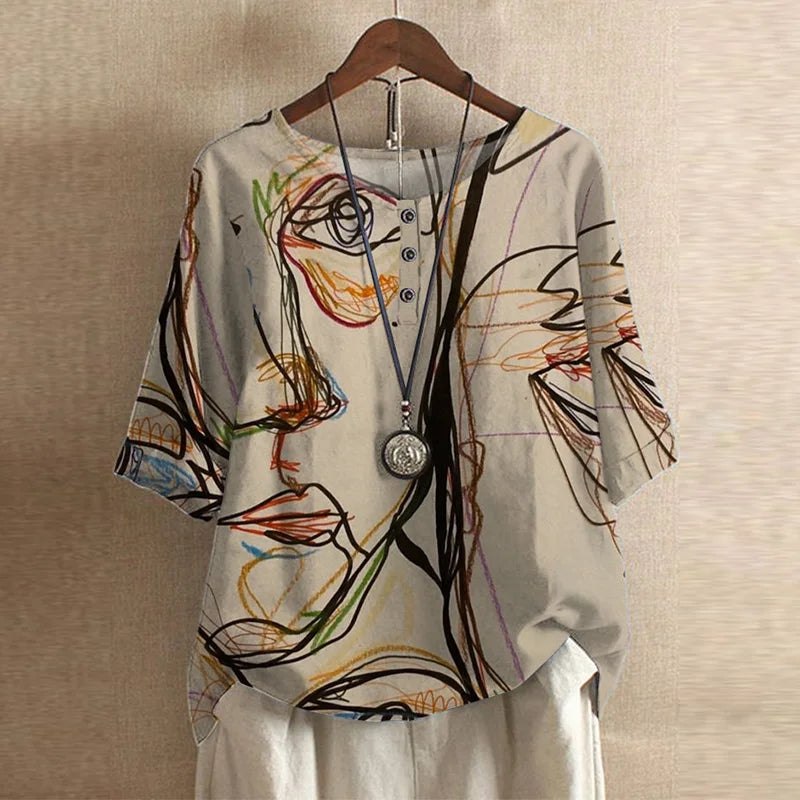 Beige short-sleeve blouse with a colorful abstract face print, button-front neckline, and a relaxed, draped fit.