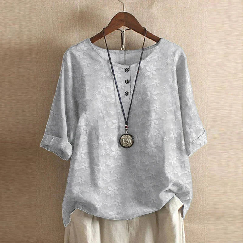 Grey floral print blouse with three-quarter sleeves, a round neckline, and a three-button front placket.