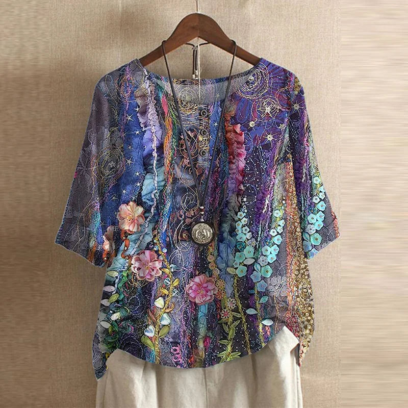 Relaxed-fit blouse with a vibrant purple floral print, round neckline, and three-quarter sleeves on a wooden hanger.