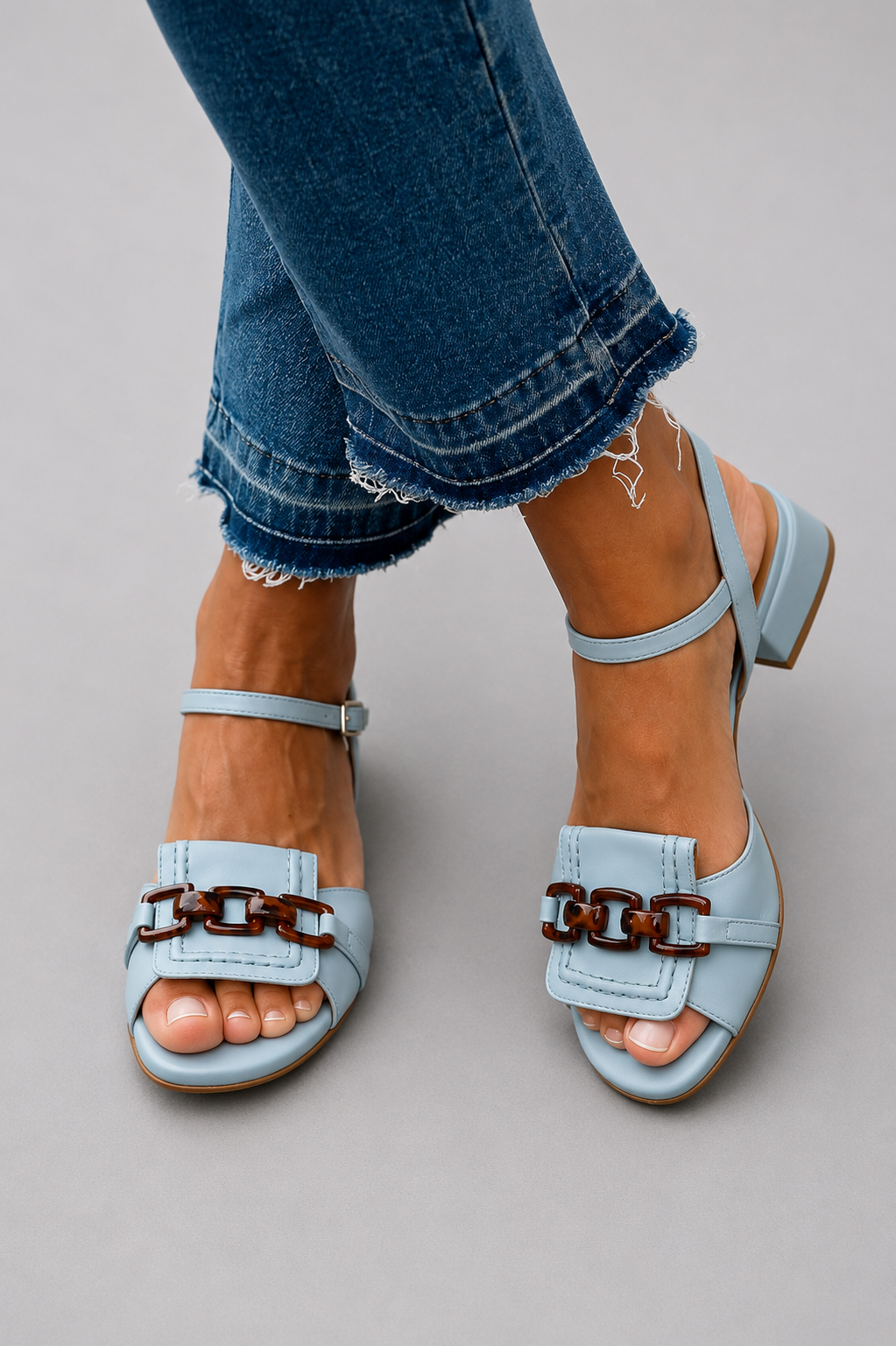 Camille sky-blue heeled sandals with tortoise shell chain detail worn with blue jeans.