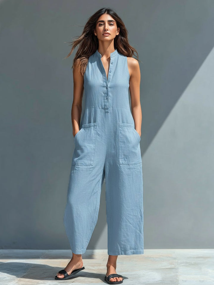 Woman in a light blue linen blend sleeveless wide-leg jumpsuit with a stand collar, button-front, and front pockets.