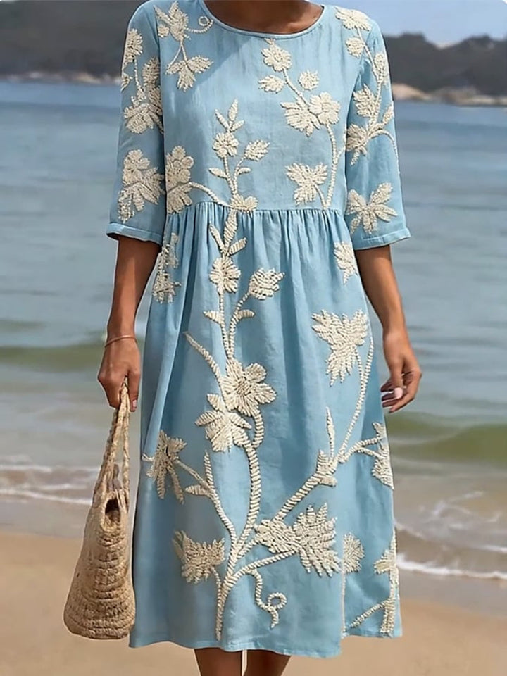 Women's light blue midi dress with white embroidered vintage floral design, three-quarter sleeves, and round neckline.