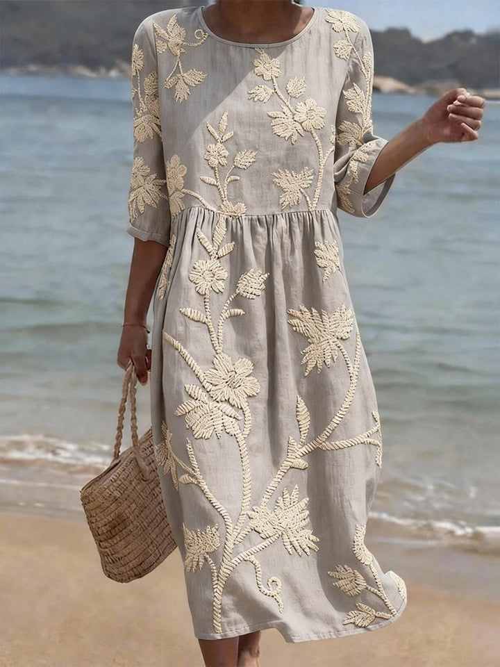 Women's Charlene vintage floral embroidered midi dress in light gray with three-quarter sleeves, worn on a beach.