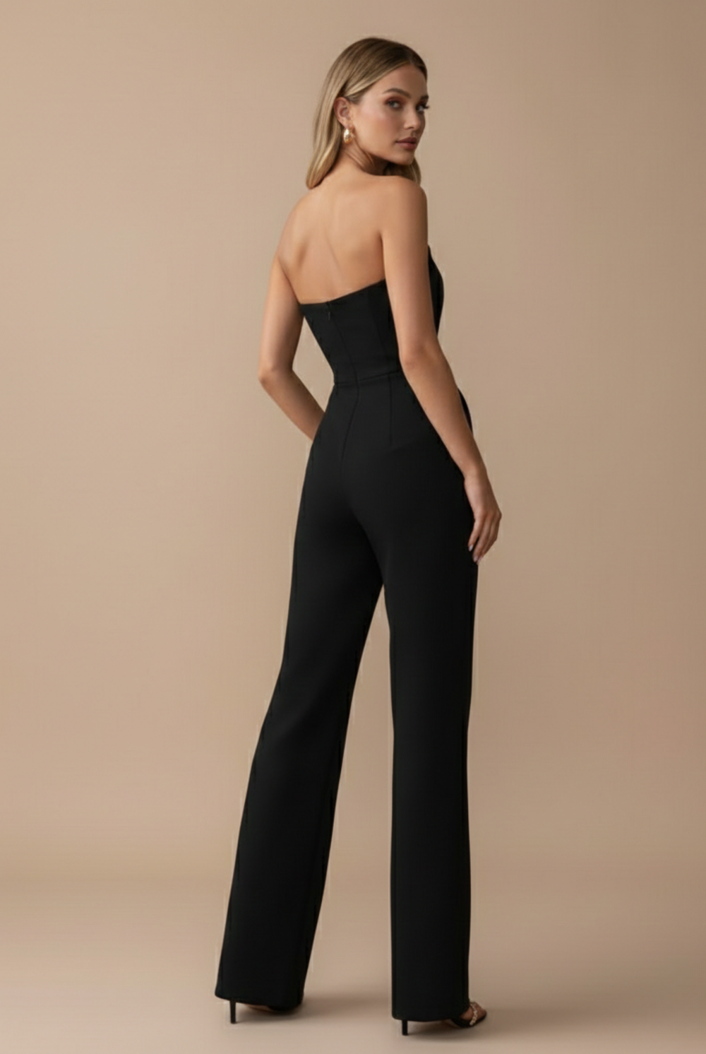 Woman in a black strapless wide-leg jumpsuit with a tailored bodice and side pockets, facing away.