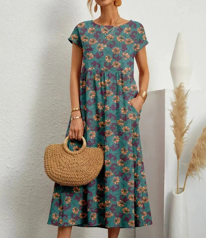 Clara women's floral cotton midi dress in vibrant teal with short sleeves and practical pockets.