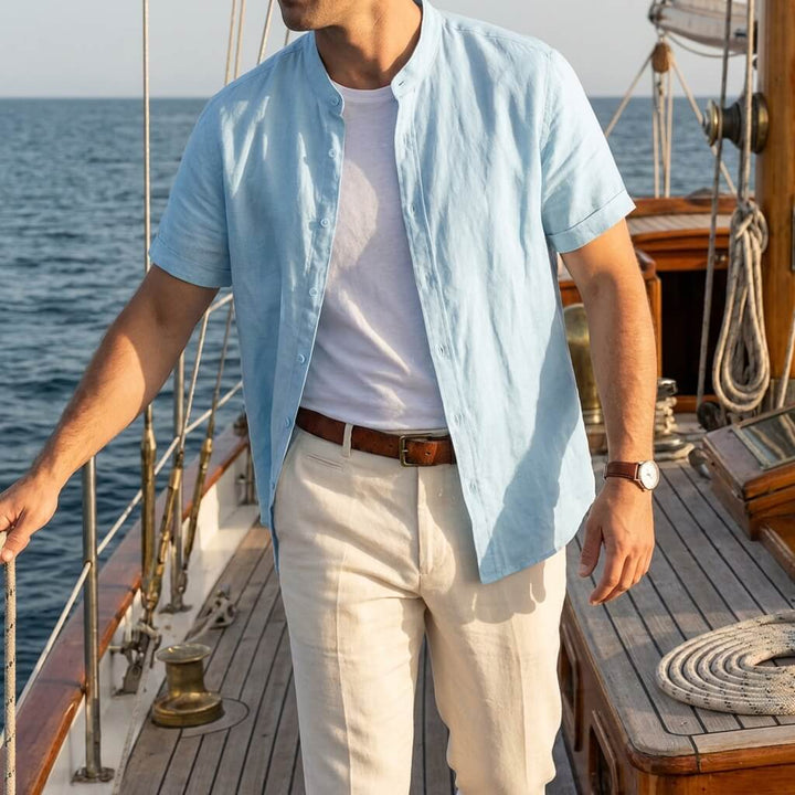 Men's Cole light blue short-sleeve linen shirt with stand collar, worn open over a white tee on a boat.