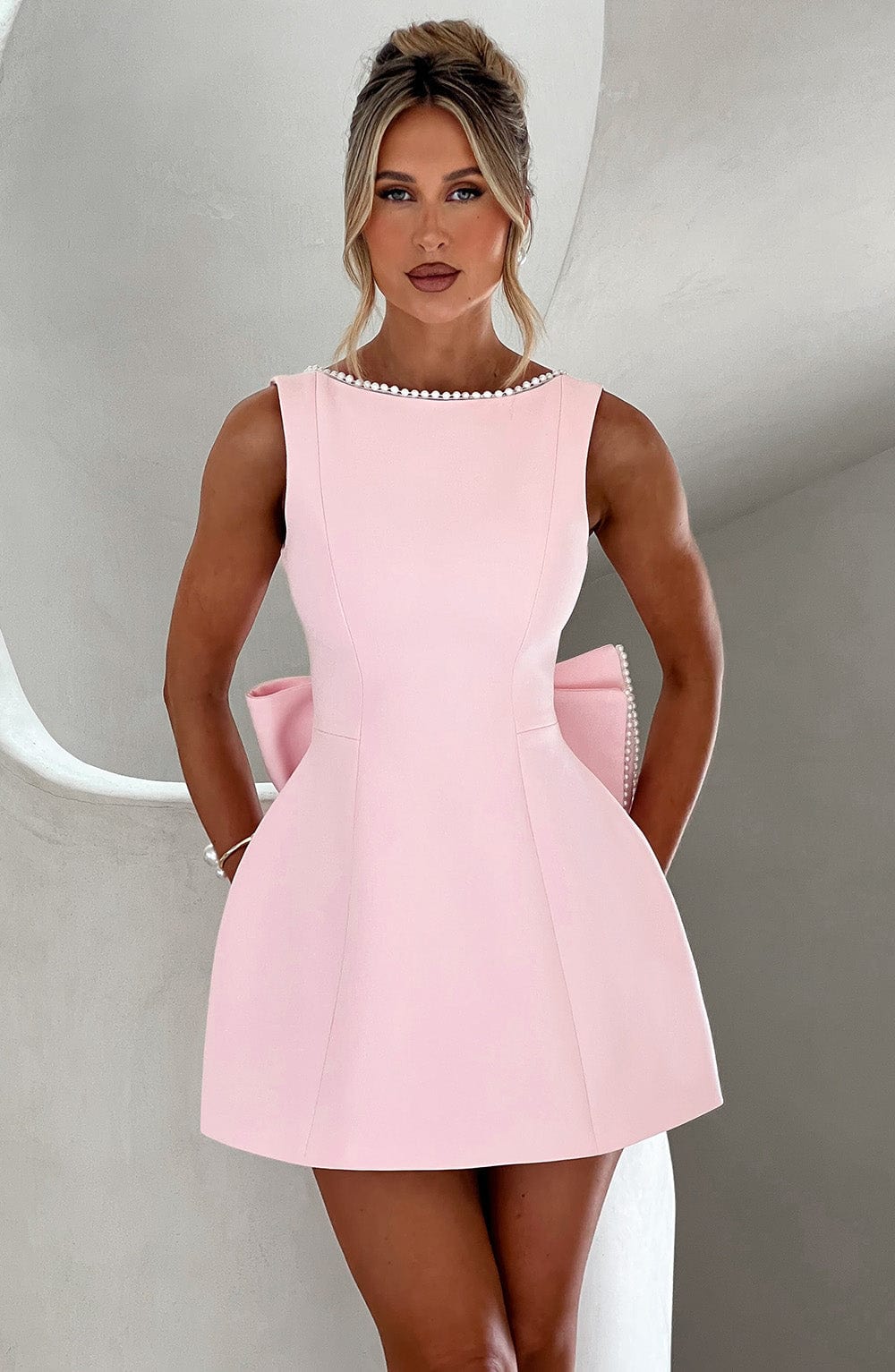 Pink Colette sleeveless structured mini dress with pearl-trimmed neckline and large back bow.
