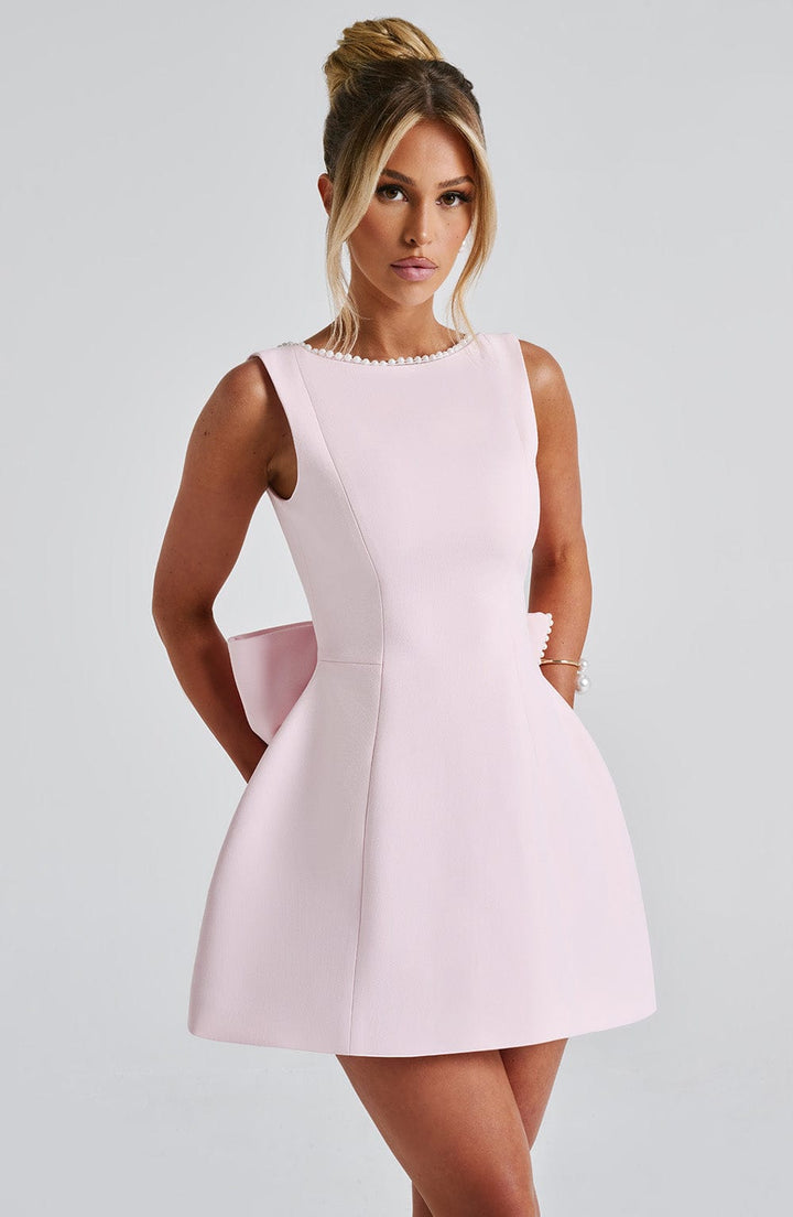 Sleeveless light pink structured mini dress with pearl trim neckline and a large back bow.