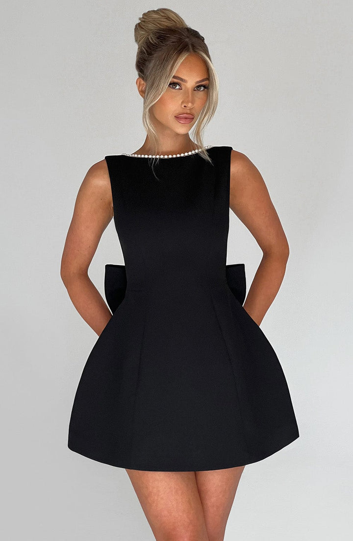 Sleeveless black structured mini dress with pearl neckline and back bow detail.