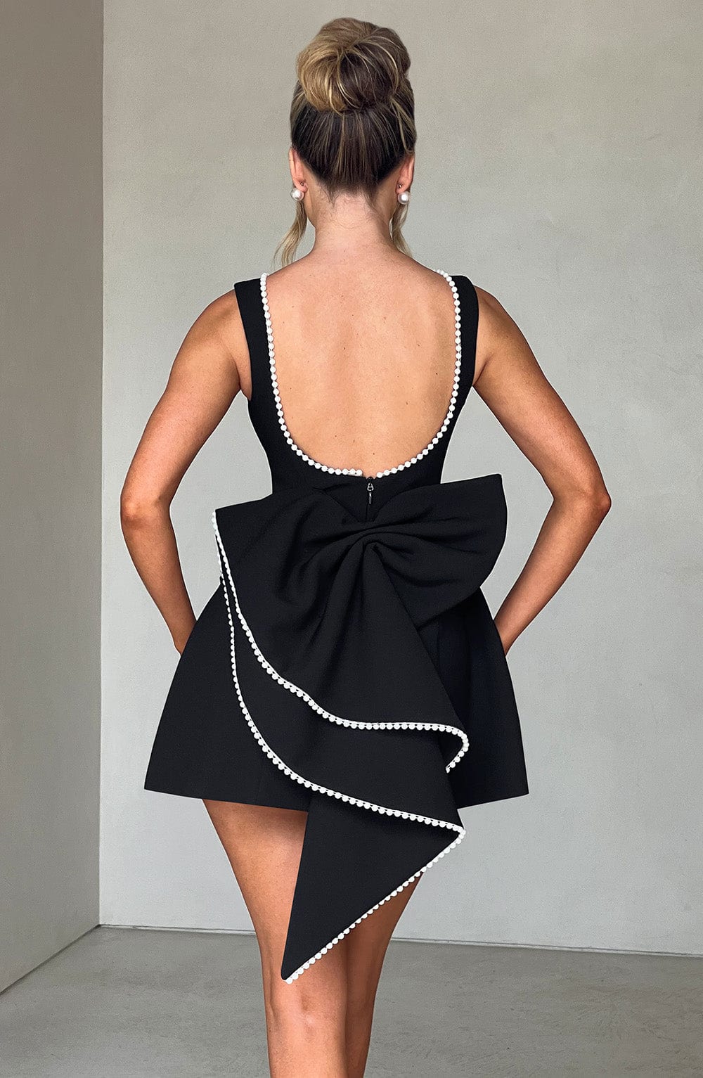Back of Colette black mini dress with low scoop back, pearl trim, and large statement bow.