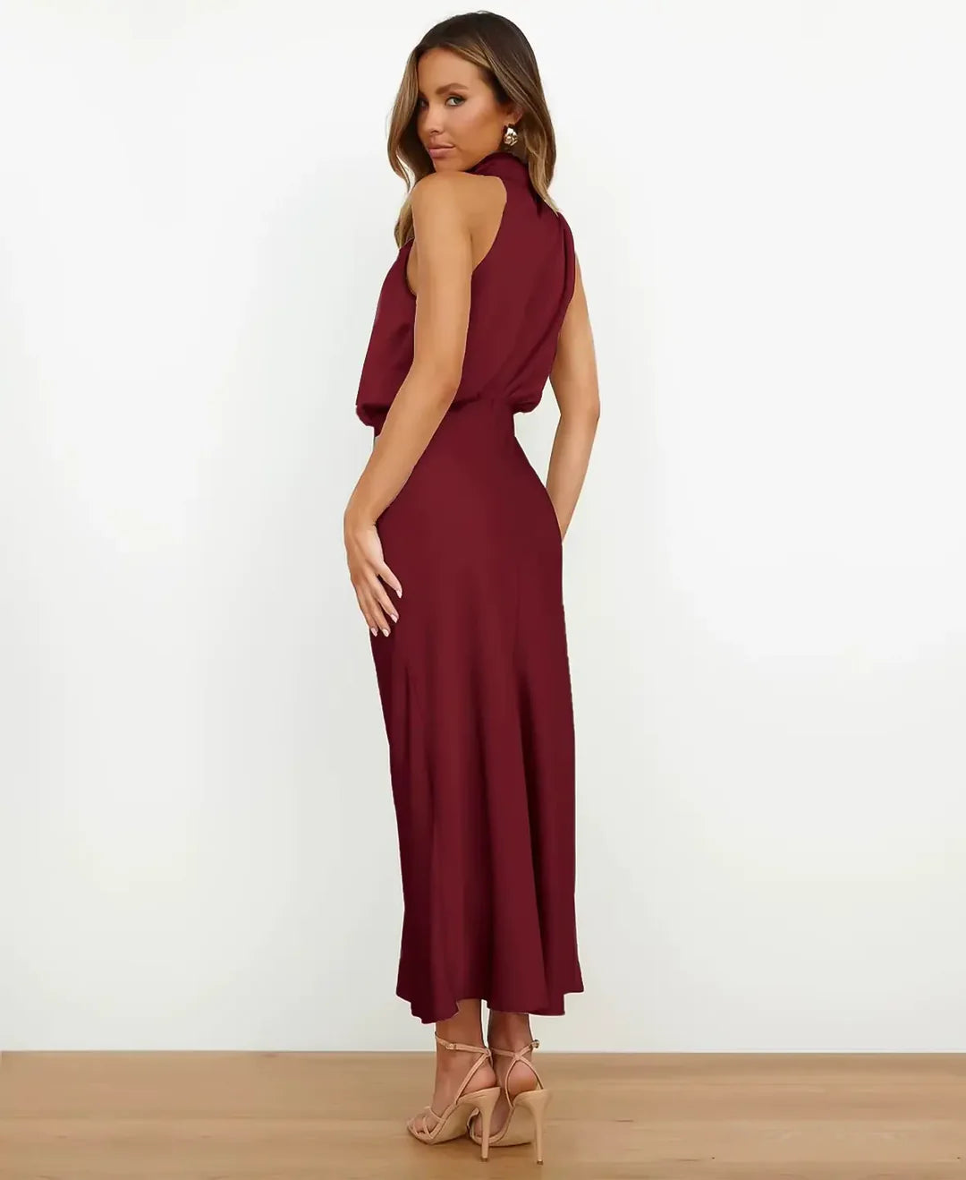 Woman in the burgundy Delphine satin halter midi dress, showing the back and side profile.