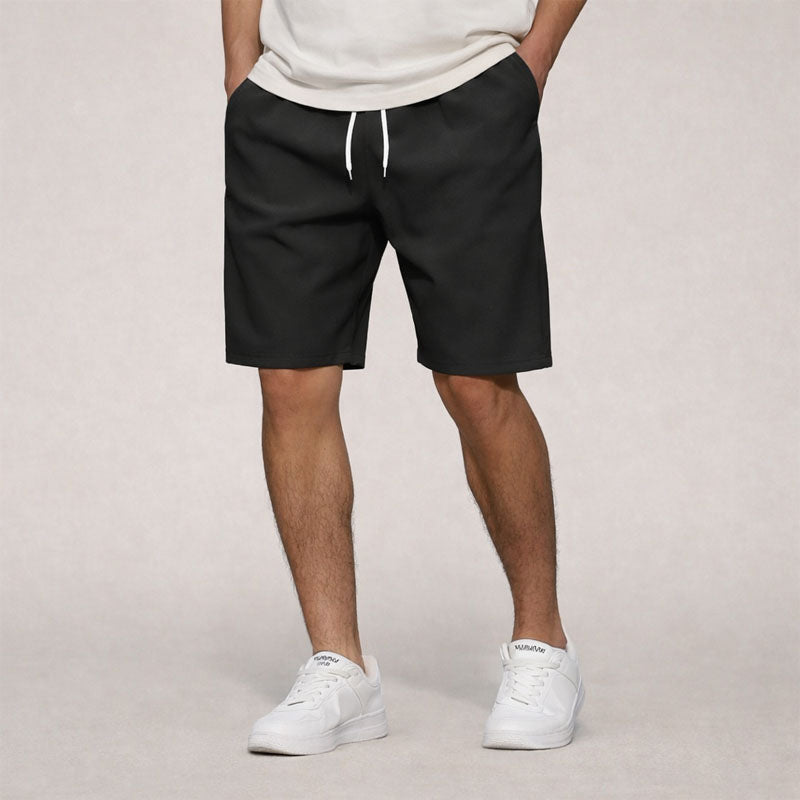 Men's black knee-length drawstring shorts with side pockets, worn with a white tee and sneakers.