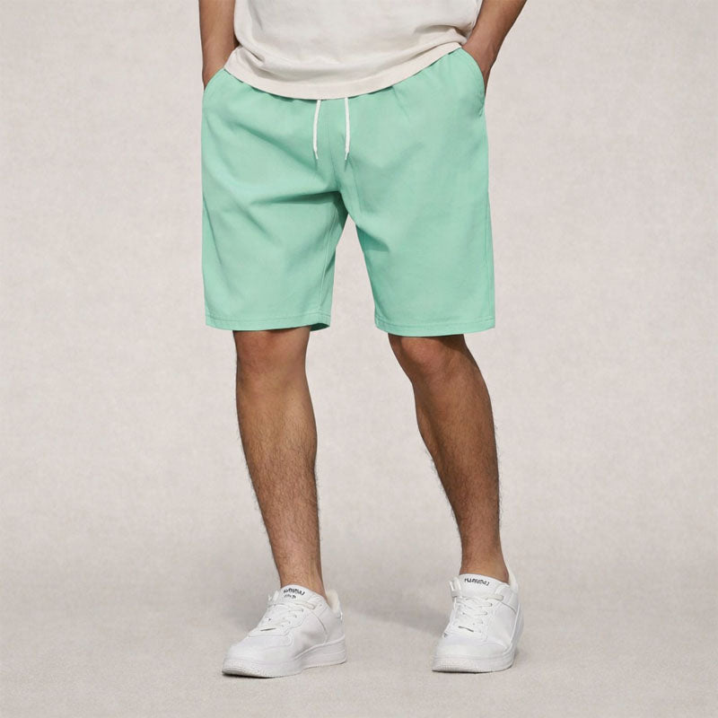 Men's mint green drawstring knee-length shorts with side pockets, paired with a light t-shirt and white sneakers.