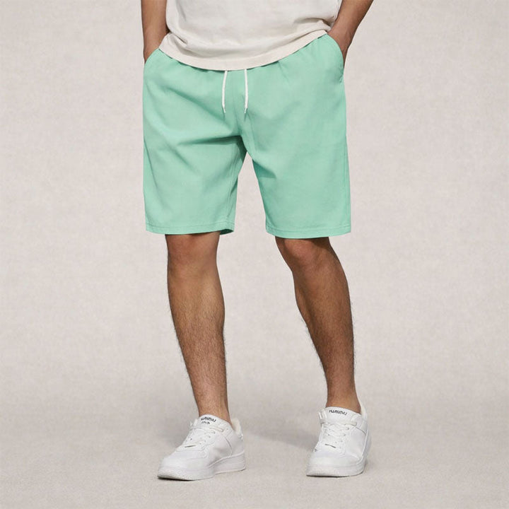 Men's mint green drawstring knee-length shorts with side pockets, paired with a light t-shirt and white sneakers.