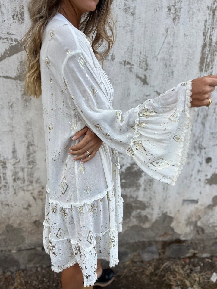 Women's white tiered boho V-neck dress with gold accents, three-quarter bell sleeves, and a relaxed fit.