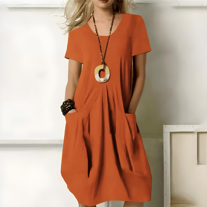 Woman wearing the Freya orange midi summer dress with short sleeves and pockets.