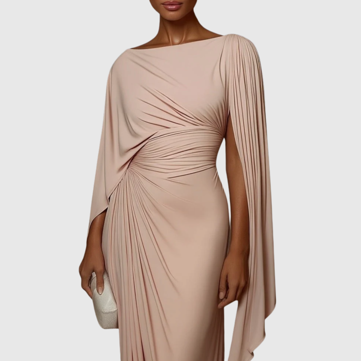 Woman in the Genevieve blush pink pleated maxi dress with elegant draped cape sleeves.