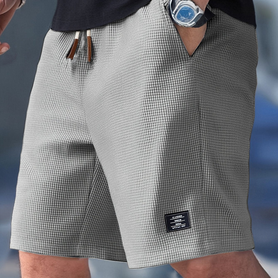 Grey waffle-knit men's shorts with an elastic drawstring waistband and a small rectangular brand patch on the hem.