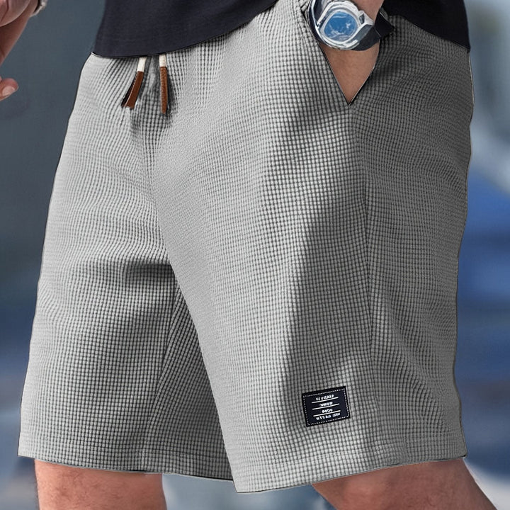 Grey waffle-knit men's shorts with an elastic drawstring waistband and a small rectangular brand patch on the hem.