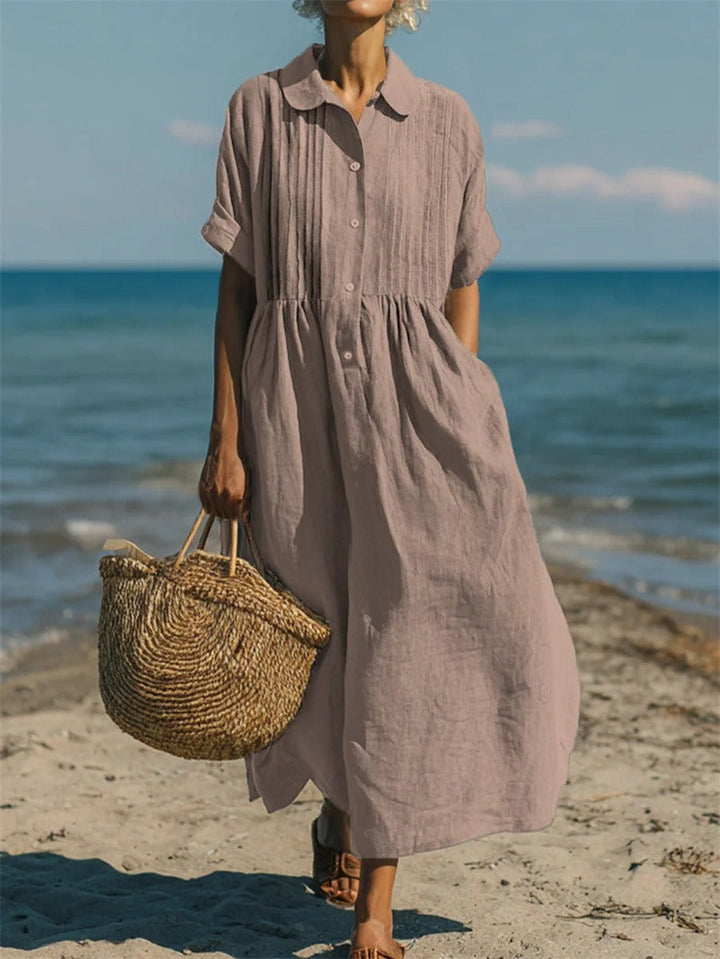 Hazel women's collared button midi dress in a relaxed, airy taupe fabric with short sleeves, walking on a beach.