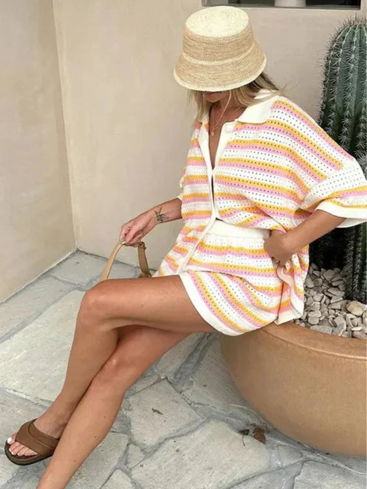 Woman in a white, pink, and yellow striped knit shorts set with a button-front top and matching shorts, wearing a straw hat.