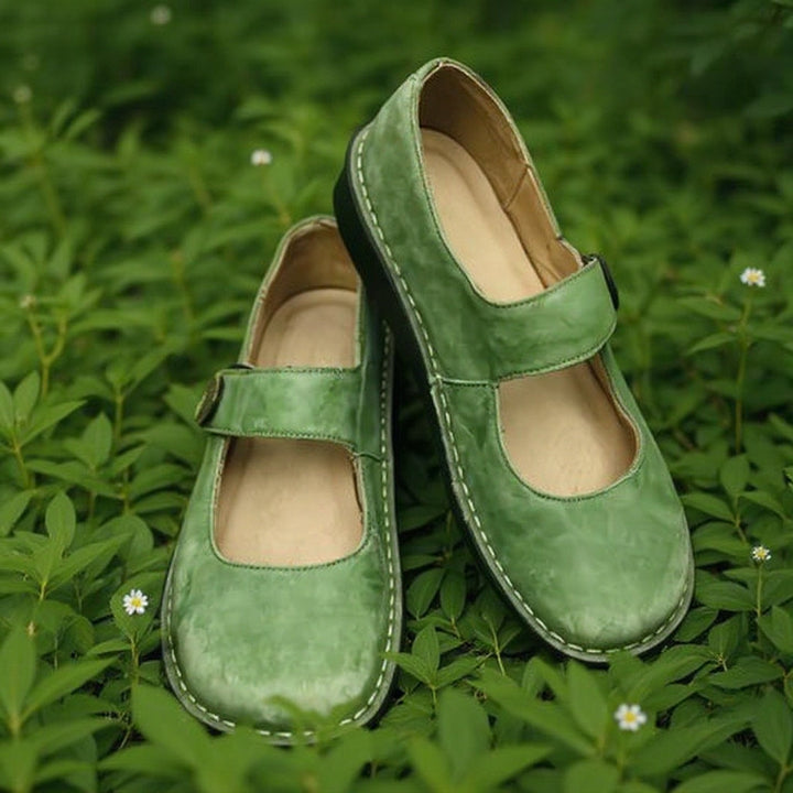 Green leather Isla Mary Jane shoes with cushioned soles on a bed of green leaves.