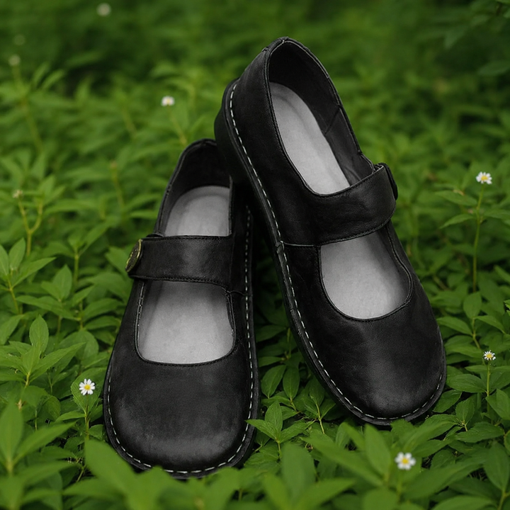 Black leather Isla Mary Jane shoes with cushioned insoles on green foliage.