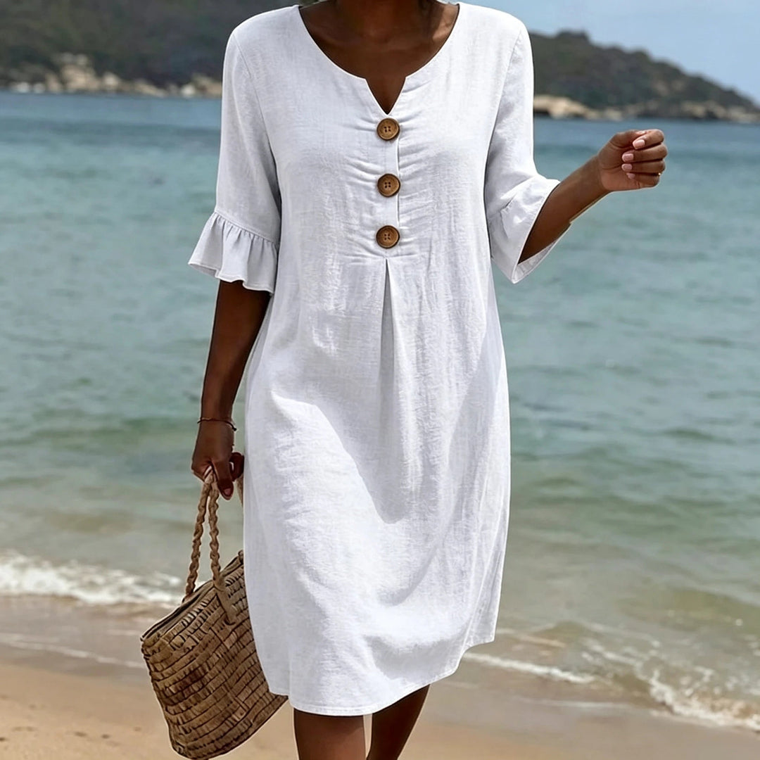 White V-neck linen midi dress with ruffle sleeves and decorative buttons, worn on a beach.
