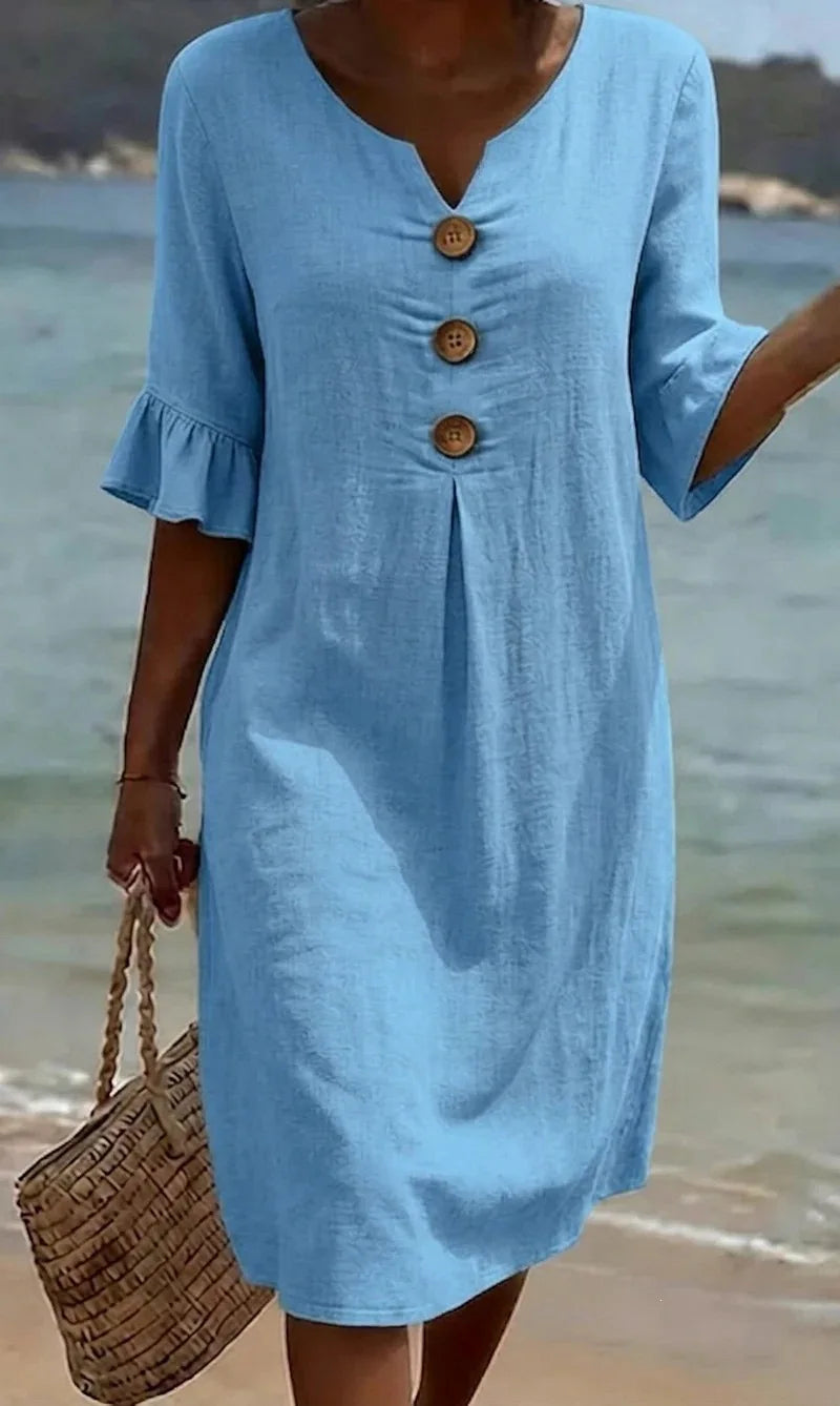 Light blue linen V-neck midi dress with ruffle sleeves and decorative buttons, worn at the beach.