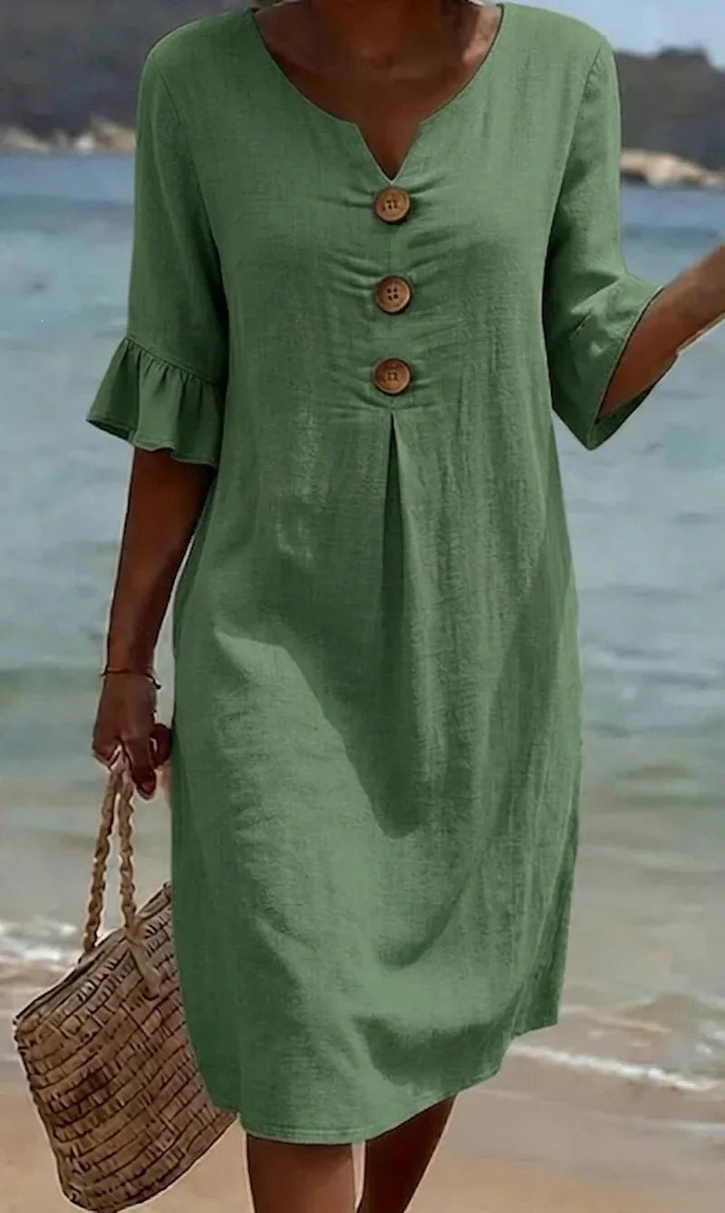 Green linen V-neck midi dress with ruffle sleeves and decorative buttons on the beach.
