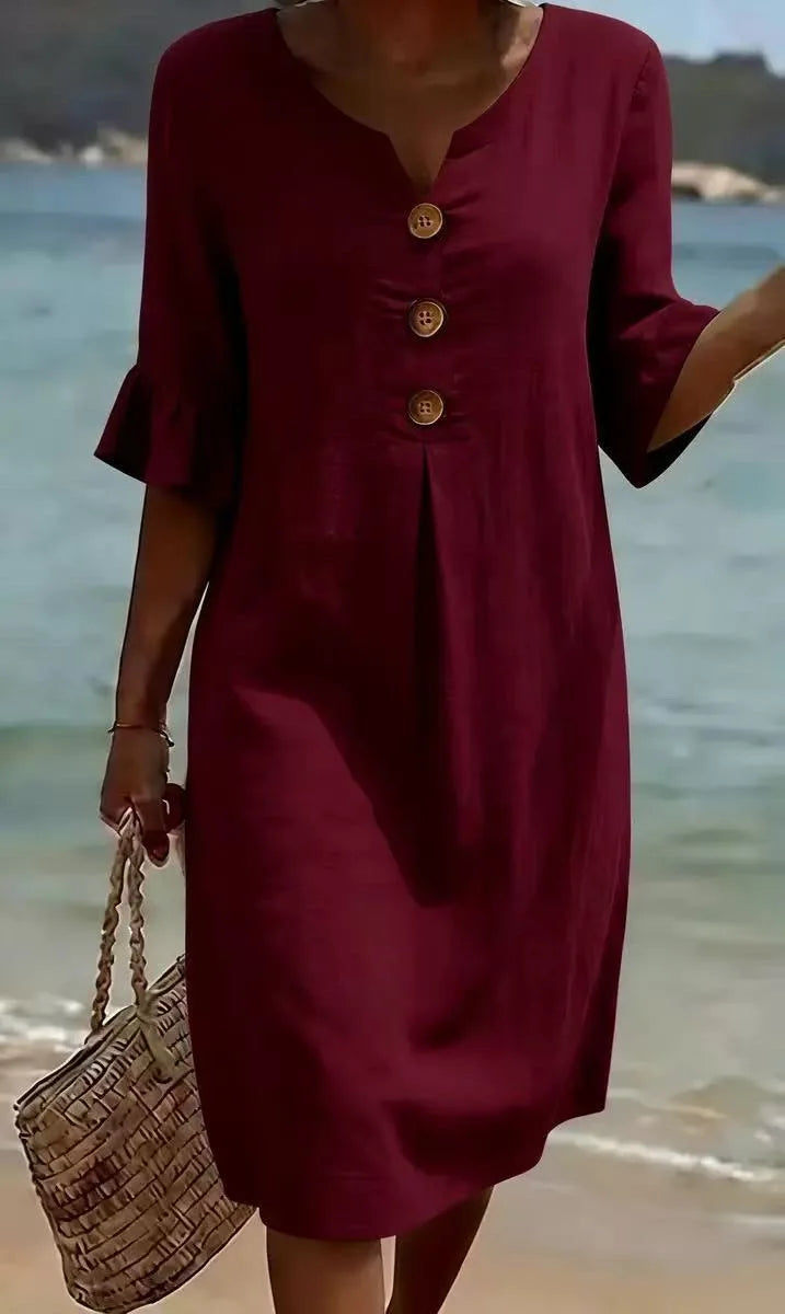 Burgundy V-neck midi dress with ruffle sleeves and three decorative buttons, worn on a beach.