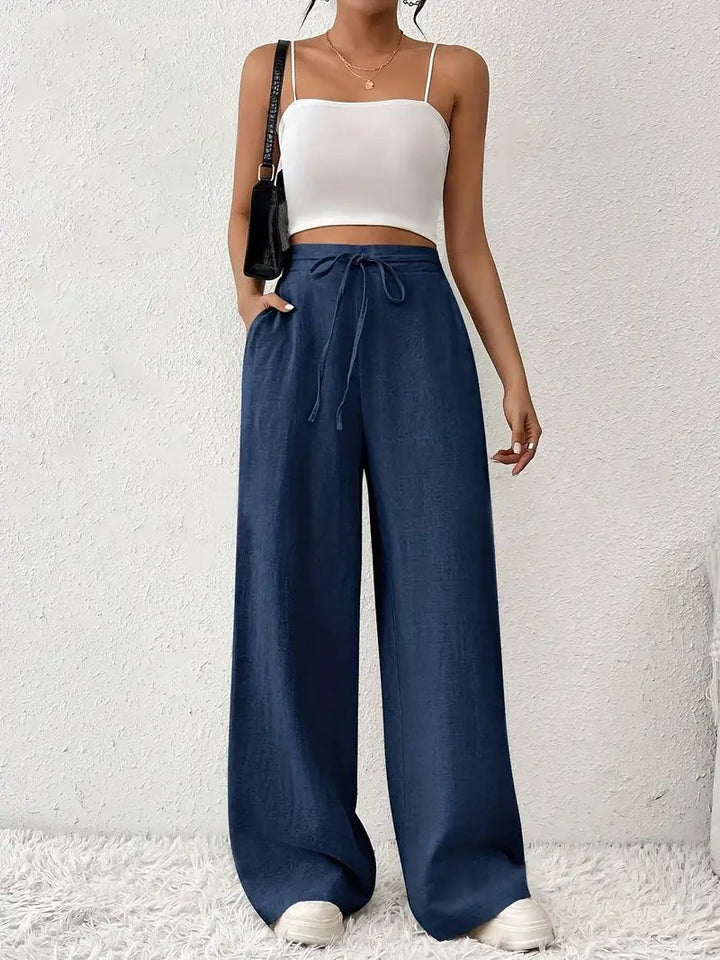 Woman wearing navy blue linen wide-leg pants with a drawstring waist and side pockets, paired with a white crop top.