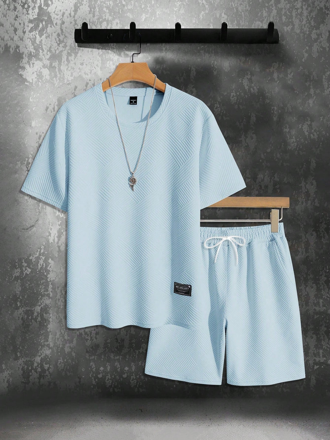 Men's light blue textured t-shirt and matching drawstring shorts set, hanging against a gray wall.