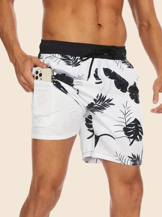 Men's Liam drawstring swim shorts in white with black tropical leaf print, featuring a side pocket.