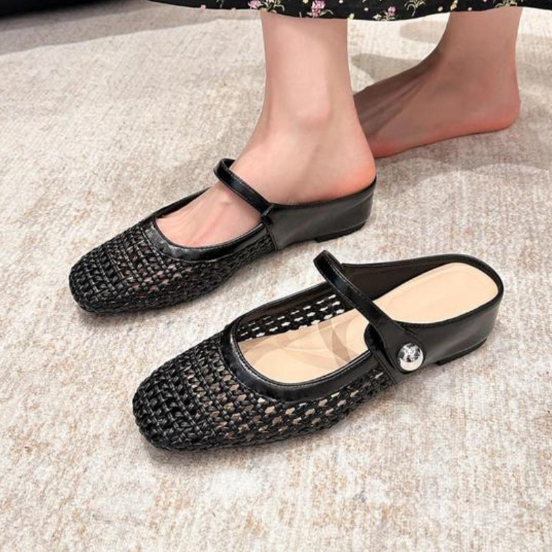Black woven flat Mary Jane slip-on mules with a silver button strap worn on feet.