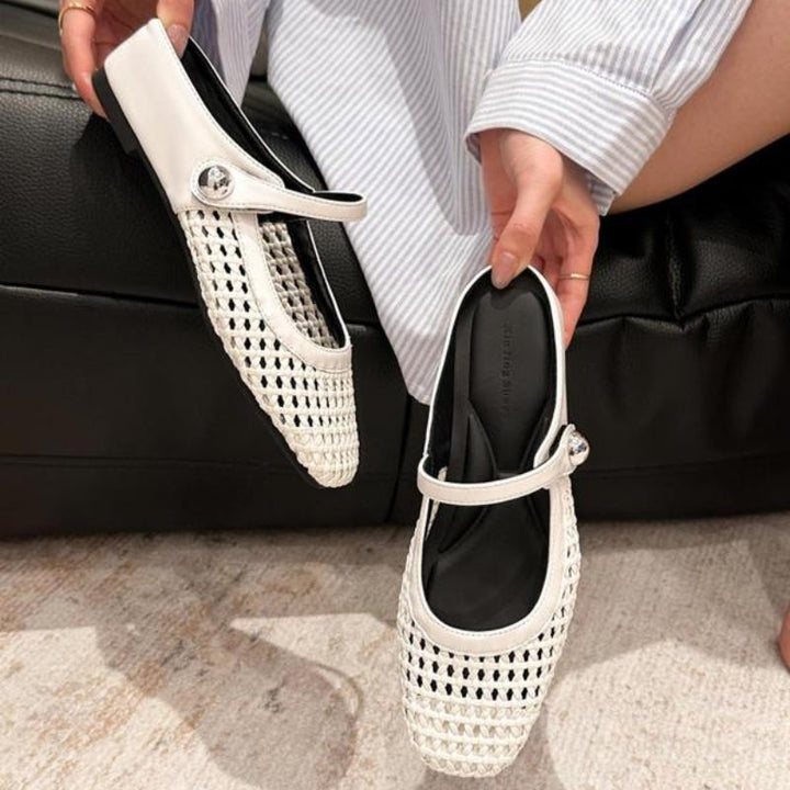 White woven Mary Jane flat mules with a silver button strap, held by a person wearing a striped shirt.